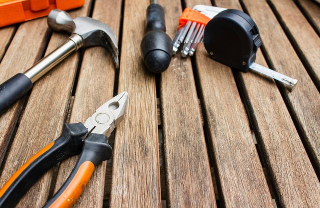 A hammer, pliers, screwdriver, hex keys and a tape measure laid out on a wooden workbench