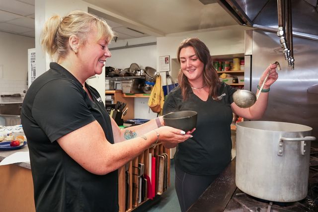 Mary-Jane handing Meghan a bowl as she ladles soup