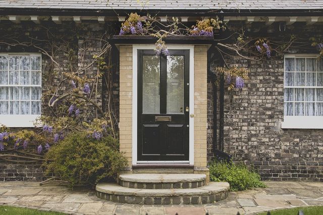 The front door and stone steps of a brick cottage, framed by wisteria